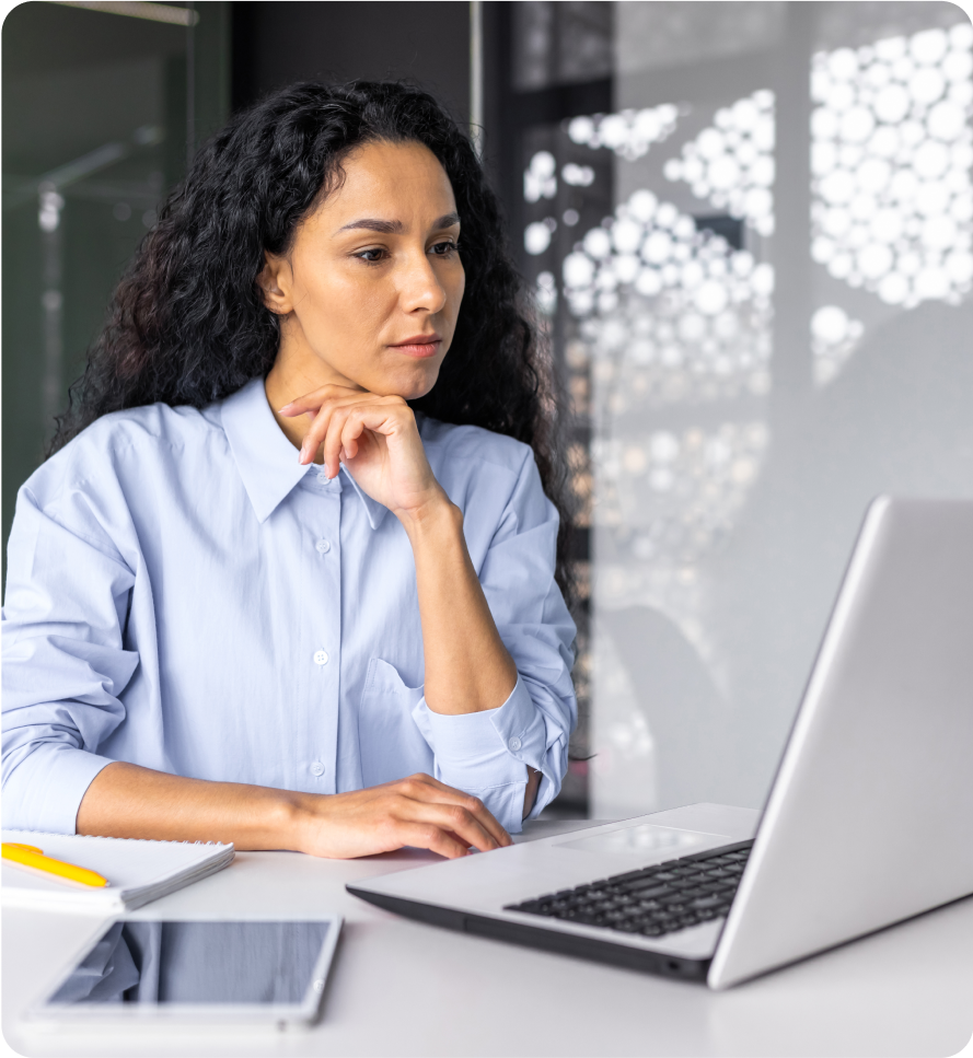 A professional woman sits at a desk viewing a laptop