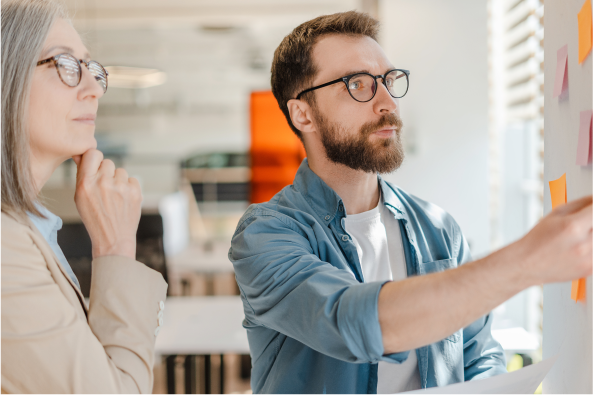 Two coworkers move sticky notes on a white board